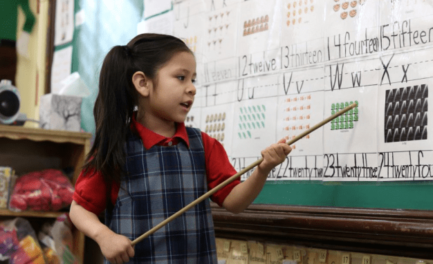 A young girl reads numbers off a poster