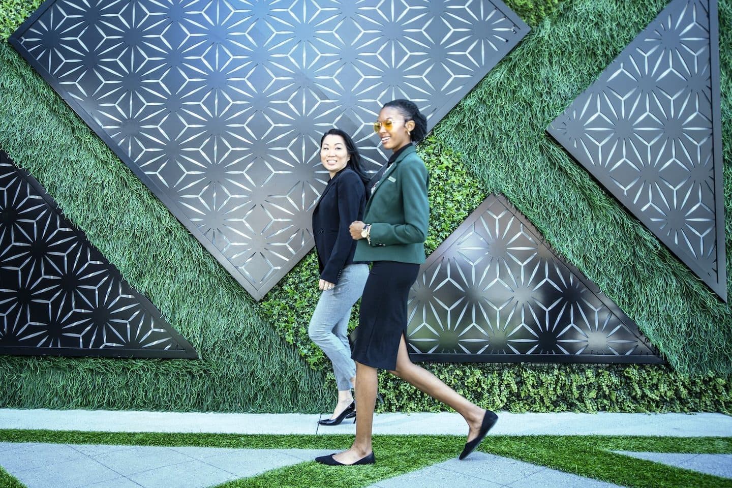 Two associates walking in front of a green wall at Aura Rooftop at the JW Marriott Charlotte