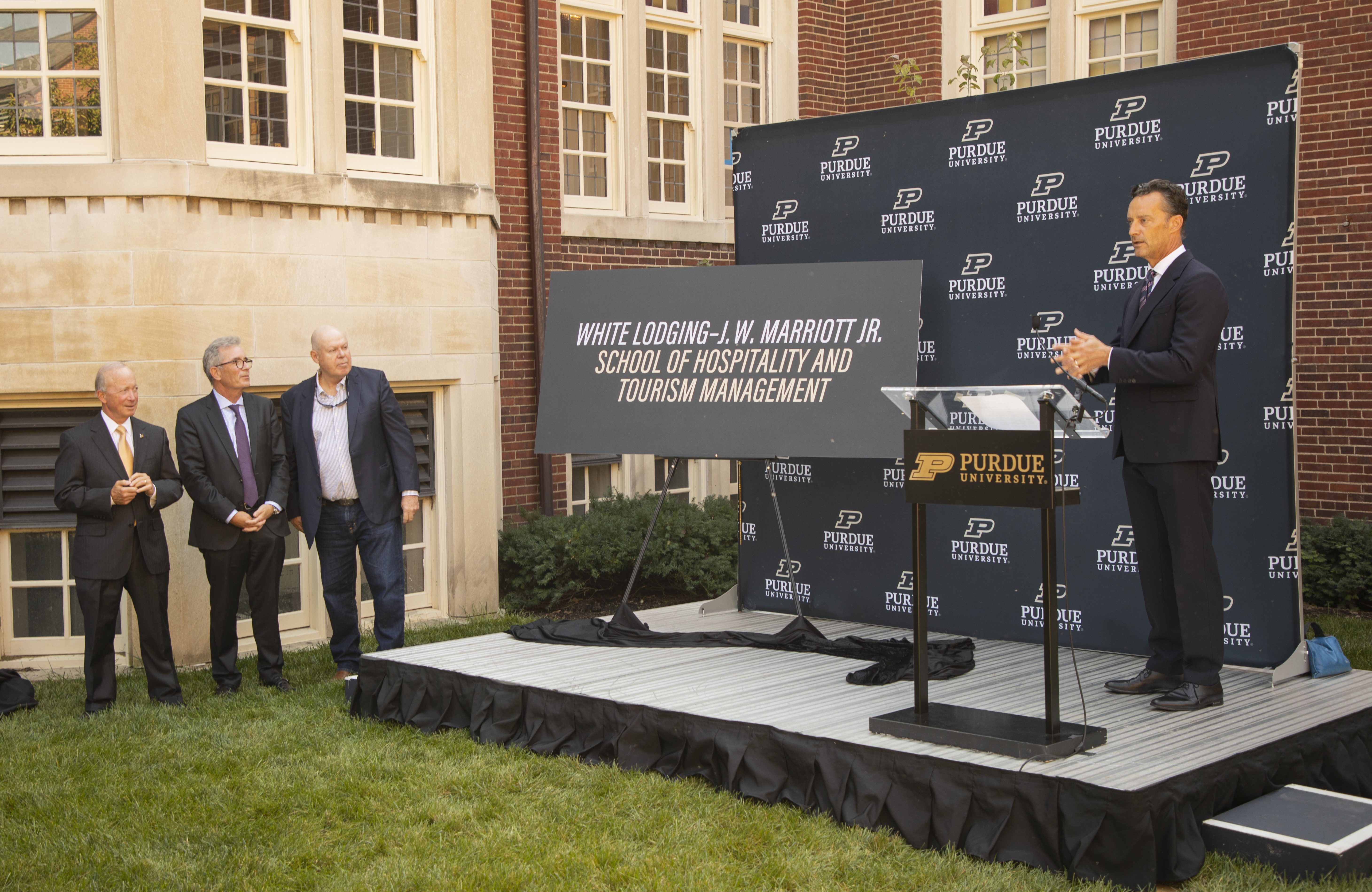 A presentation at Purdue University for the White Lodging-J.W. Marriott School of Hospitality and Tourism Management, where one man in a suit stands behind a podium onstage.