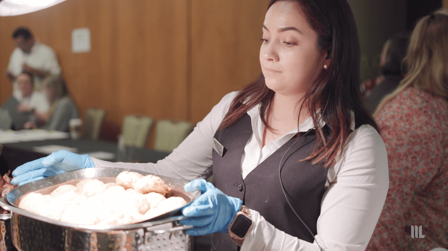 waitress wearing gloves holding a metal pot of food